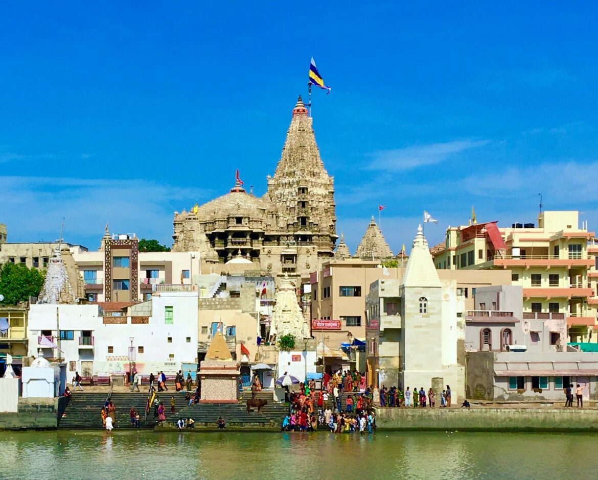 The grand multi-storied Dwarkadhish Temple in Dwarka, with its magnificent flag (Dhwaja) flying high, seen from the Gomti Ghat during the monsoon season of Shravan.