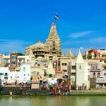 The grand multi-storied Dwarkadhish Temple in Dwarka, with its magnificent flag (Dhwaja) flying high, seen from the Gomti Ghat during the monsoon season of Shravan.