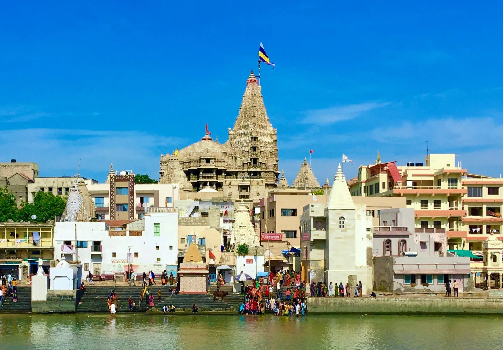 The grand multi-storied Dwarkadhish Temple in Dwarka, with its magnificent flag (Dhwaja) flying high, seen from the Gomti Ghat during the monsoon season of Shravan.